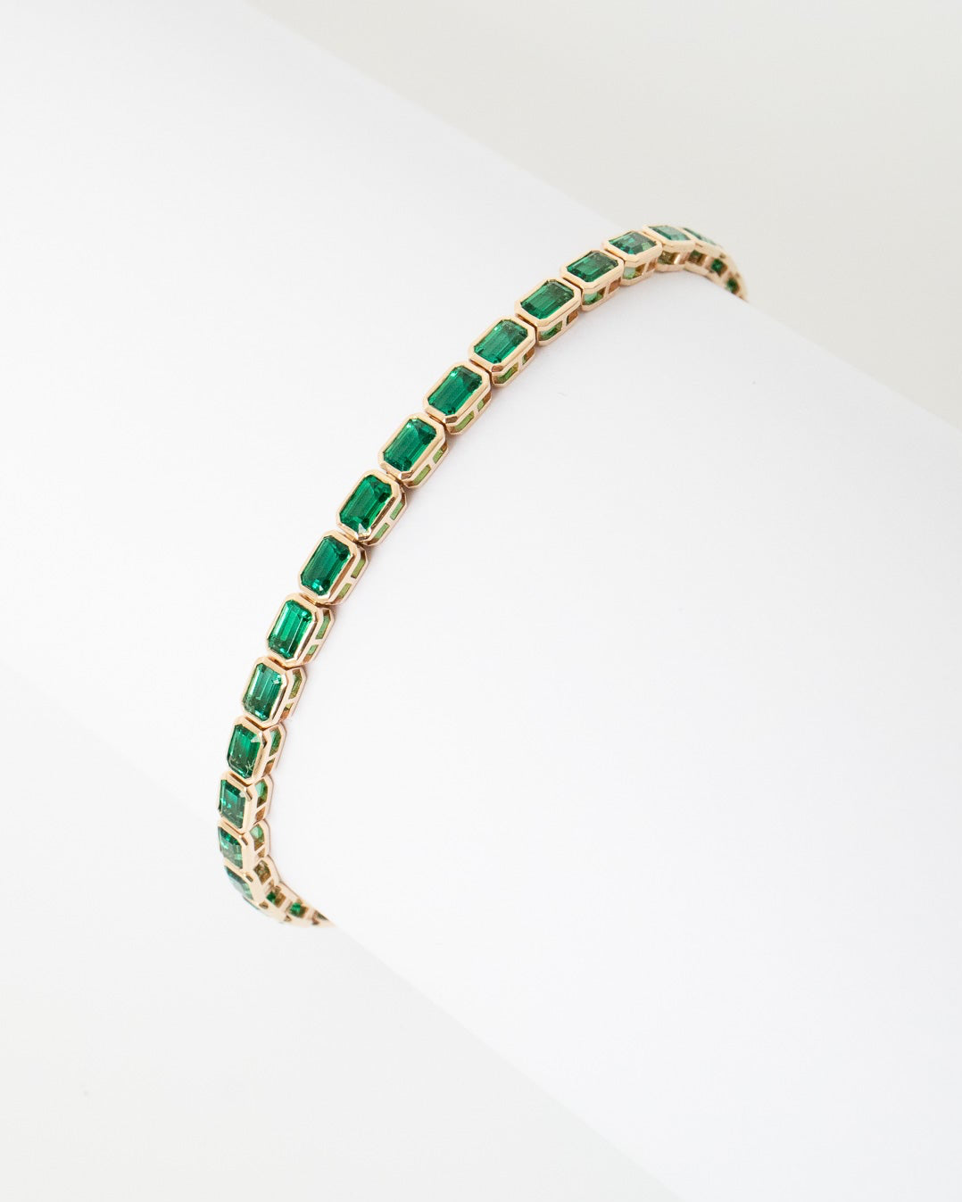 Gold bracelet with green gemstones on a white background