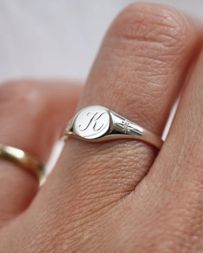 Silver ring with a monogram on a person's finger against a neutral background