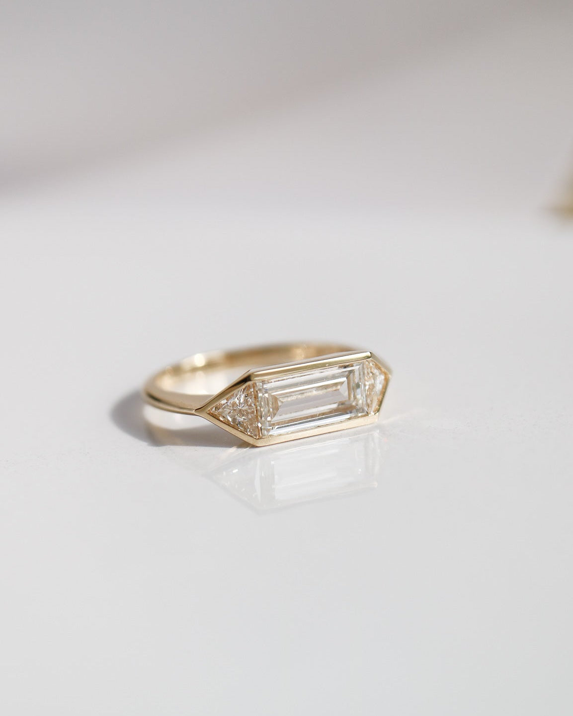 Gold ring with a baguette cut gemstone on a light gray background