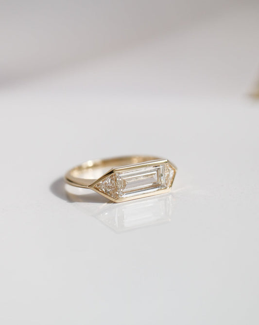 Gold ring with a baguette cut gemstone on a light gray background