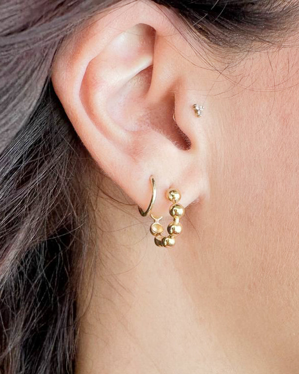 Close-up of an ear wearing gold hoop and bead earrings.