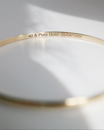 Gold bracelet with engraved text on a light gray background