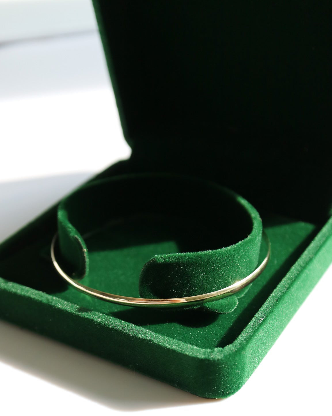 Gold ring in a green jewelry box on a white surface