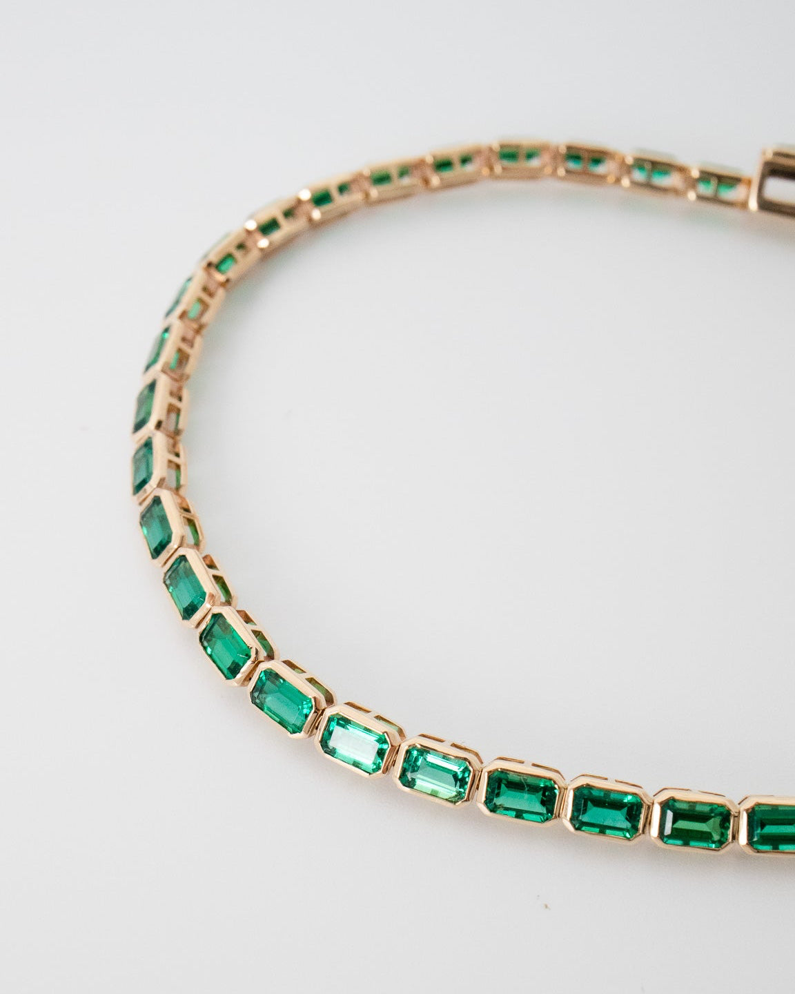 Gold bracelet with green gemstones on a light gray background