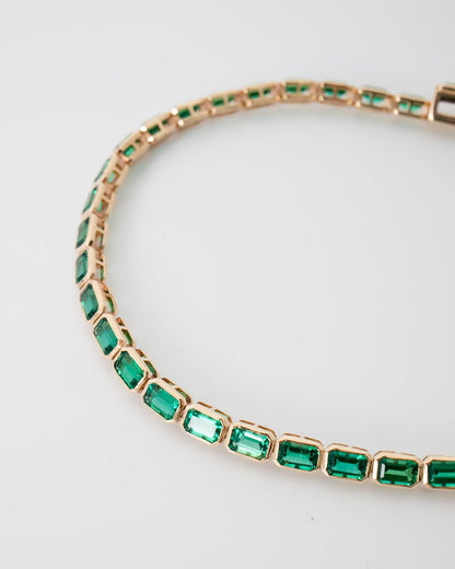 Gold bracelet with green gemstones on a light gray background