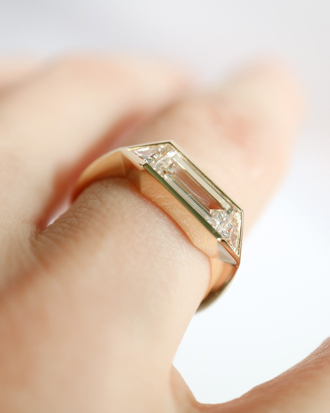 Gold ring with a diamond on a finger against a light background