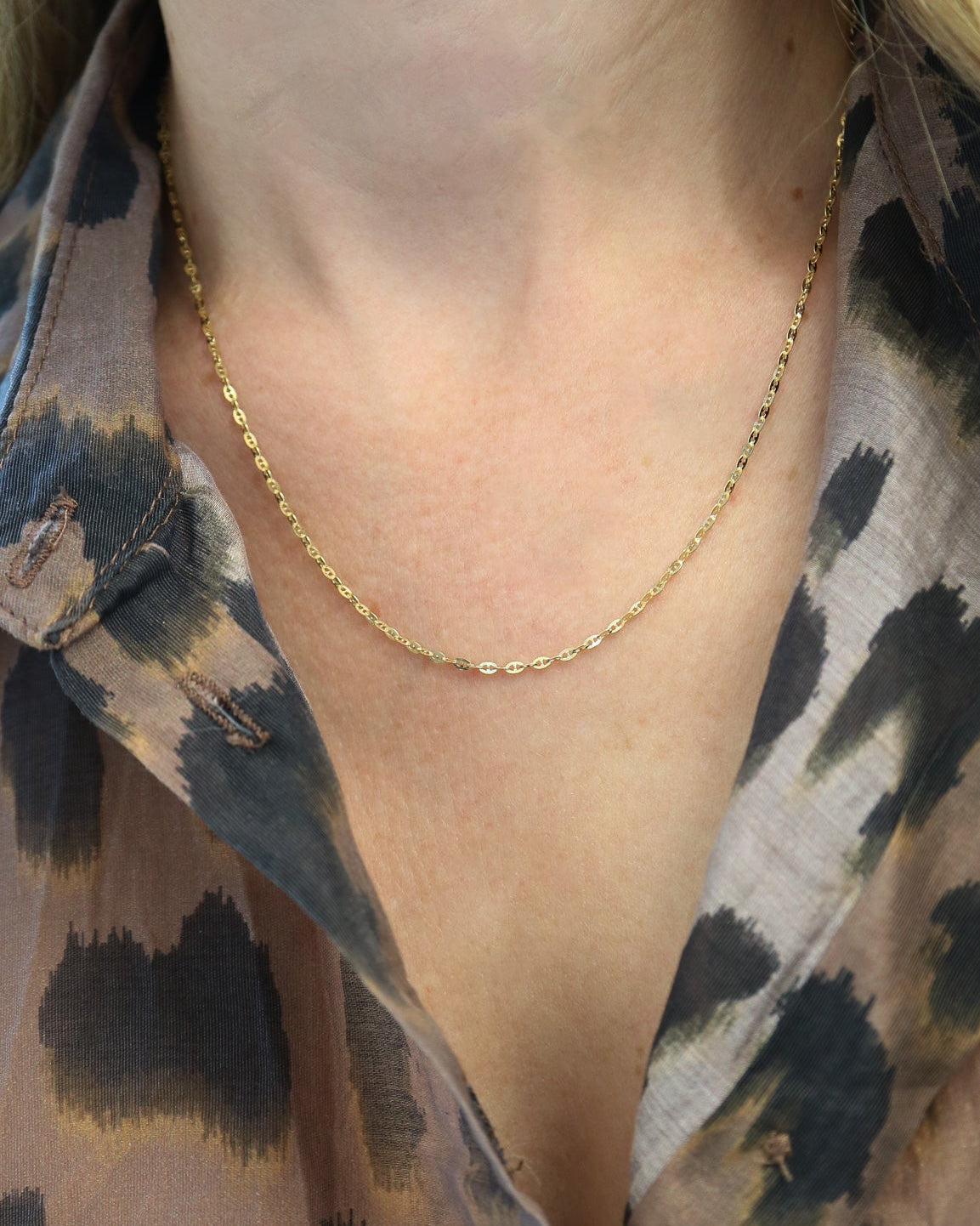 
9kt solid gold Mini Gucci Link Chain necklace on a white background, showcasing its delicate interlocking links and polished gold finish on female neck wearing leopard print shirt