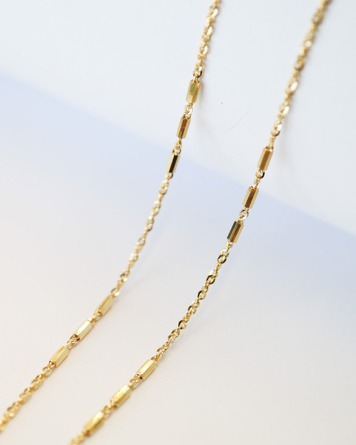 9kt solid gold Morse Code Chain necklace featuring a delicate gold chain with polished rectangular bar accents, photographed on an off-white background close up detail