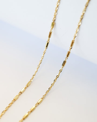 9kt solid gold Morse Code Chain necklace featuring a delicate gold chain with polished rectangular bar accents, photographed on an off-white background close up detail