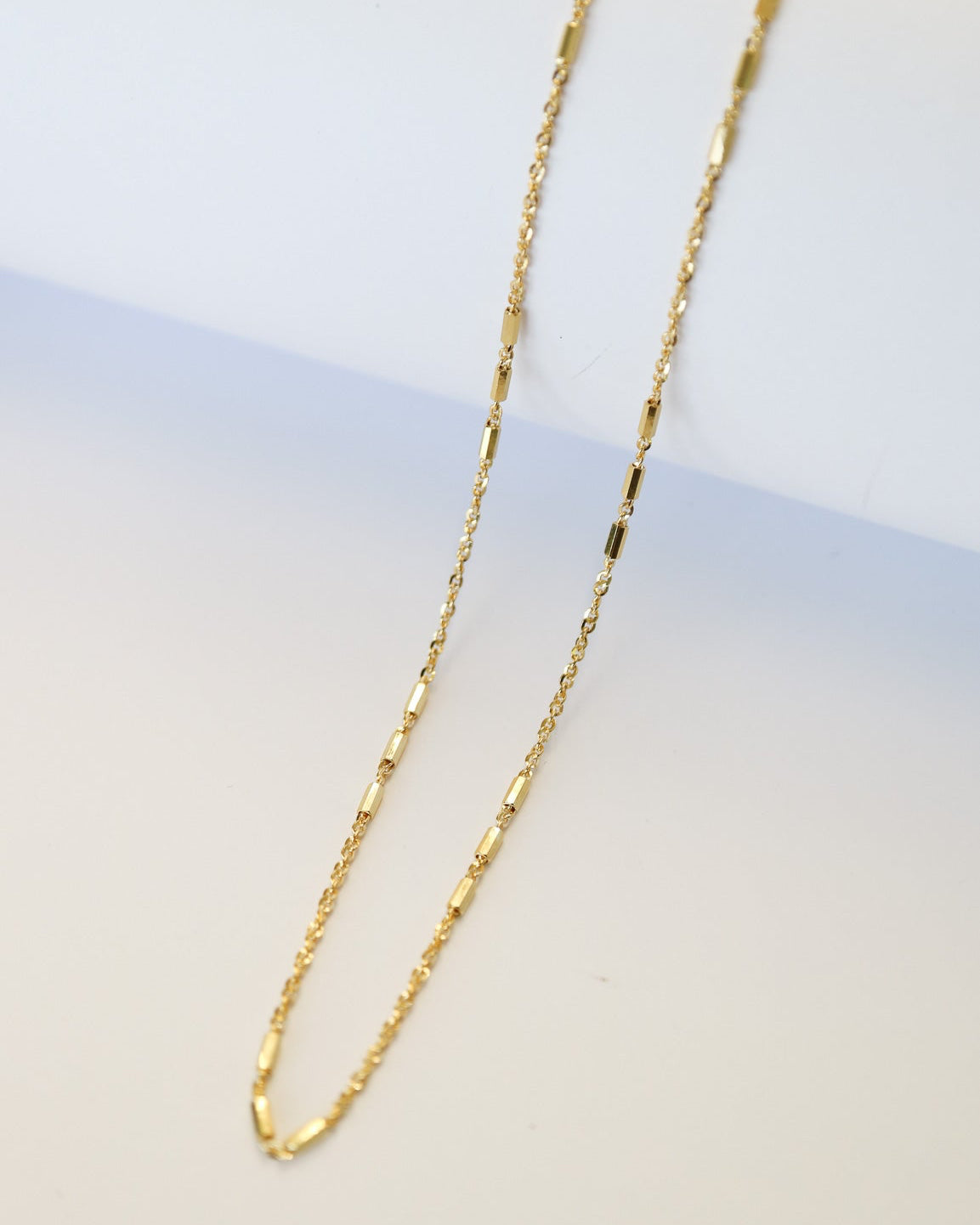 9kt solid gold Morse Code Chain necklace featuring a delicate gold chain with polished rectangular bar accents, photographed on an off-white background.