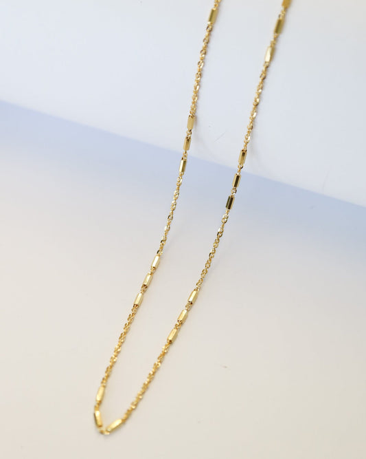 9kt solid gold Morse Code Chain necklace featuring a delicate gold chain with polished rectangular bar accents, photographed on an off-white background.