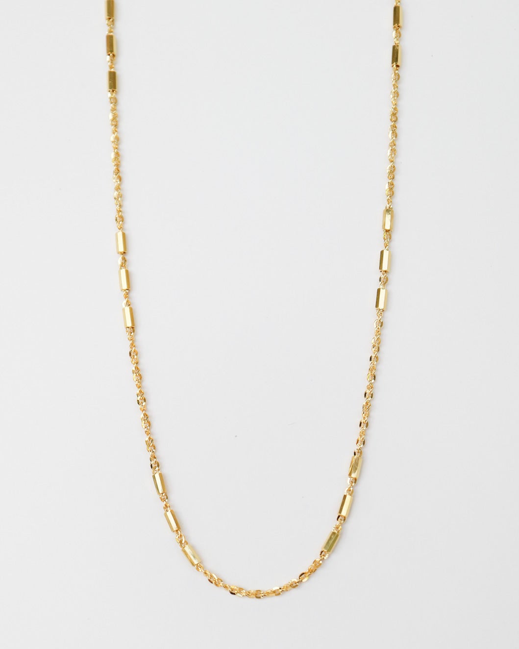 9kt solid gold Morse Code Chain necklace featuring a delicate gold chain with polished rectangular bar accents, photographed on an off-white background.