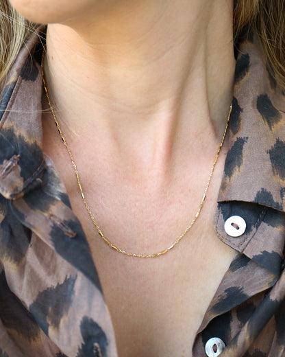 9kt solid gold Morse Code Chain necklace featuring a delicate gold chain with polished rectangular bar accents, photographed on female neck