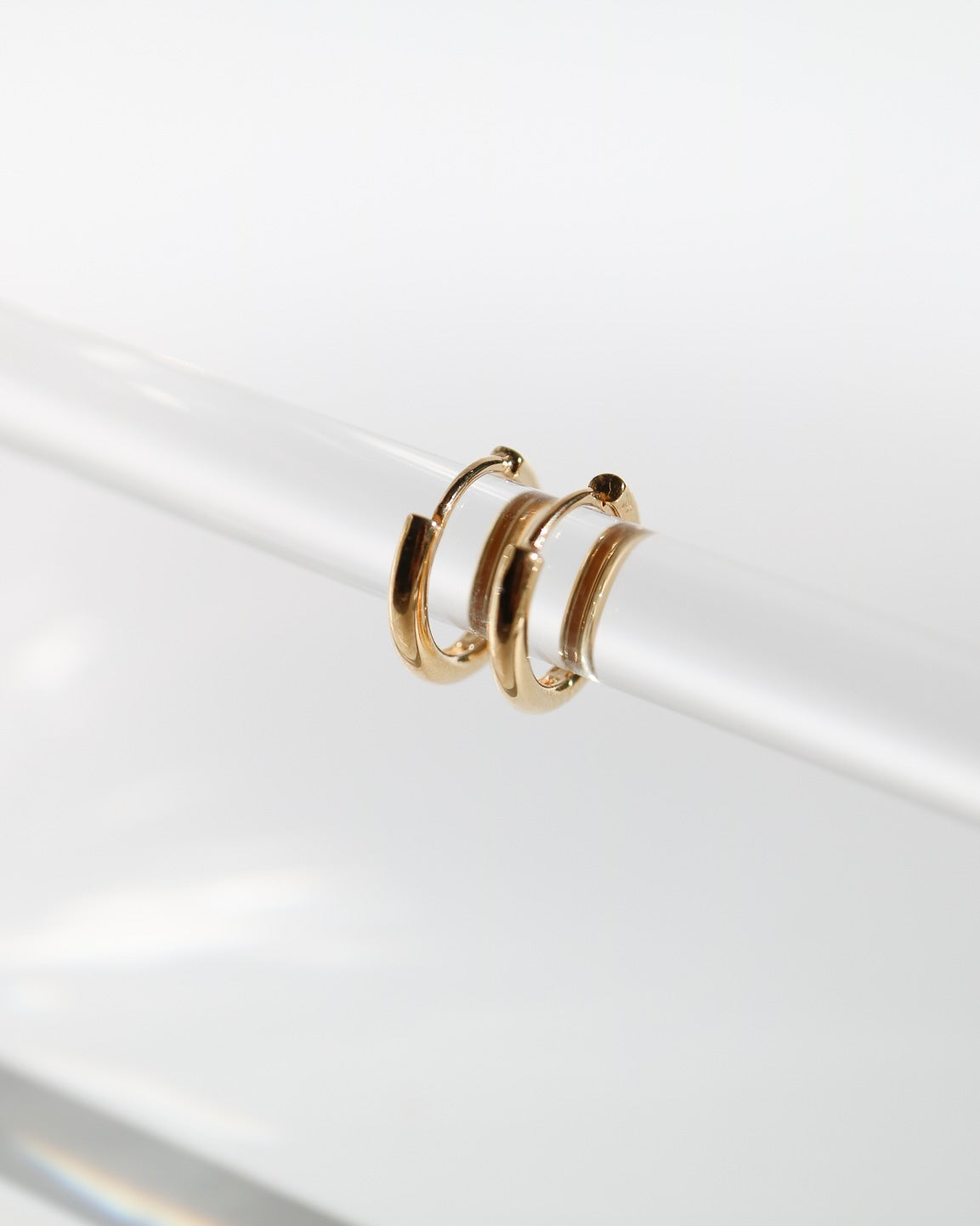 Pair of 9kt solid gold Rounded Huggie Earrings with a polished finish and classic circular design, shown worn on a clear rod
