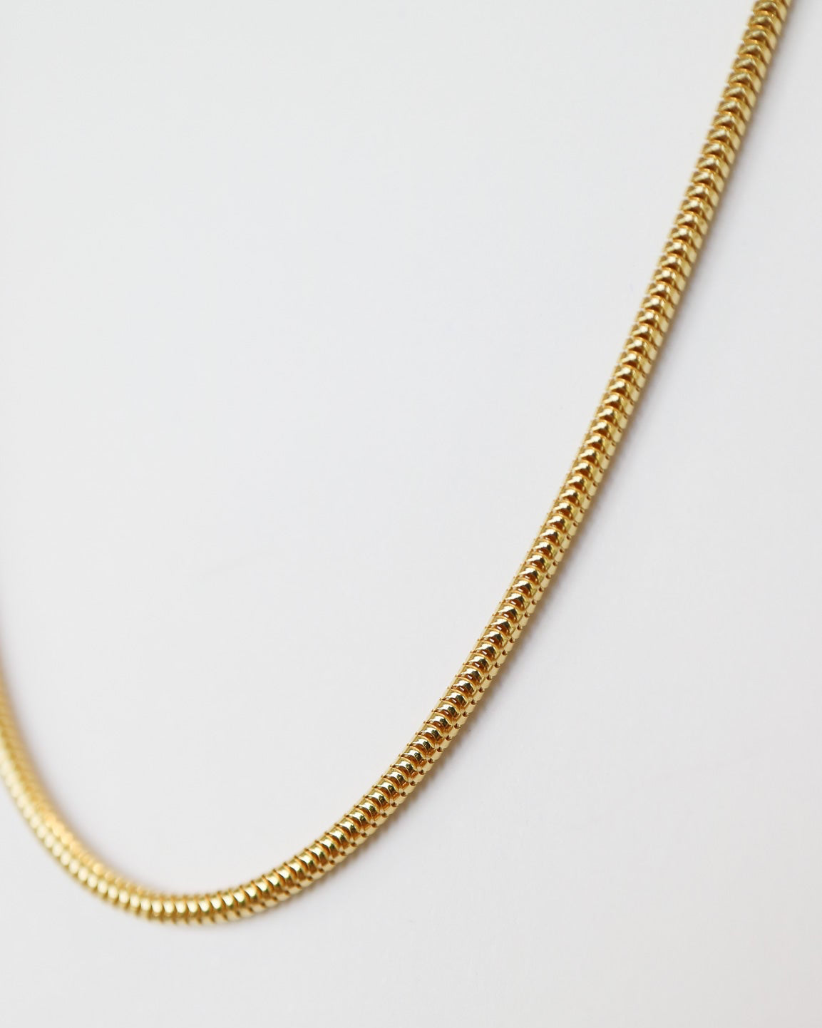 9ct solid gold skinny snake chain necklace with a delicate, flexible design and polished gold finish, photographed on an off-white background close up