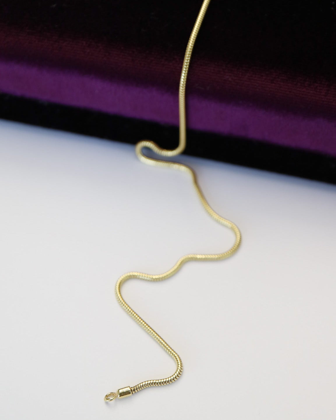 9ct gold Skinny Real Snake Chain draped over purple velvet jewellery box