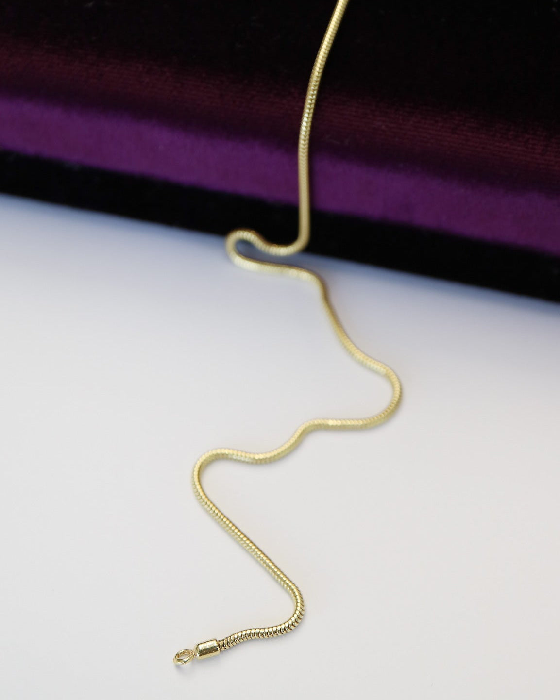 9ct solid gold skinny snake chain necklace with a delicate, flexible design and polished gold finish, photographed on an off-white background.