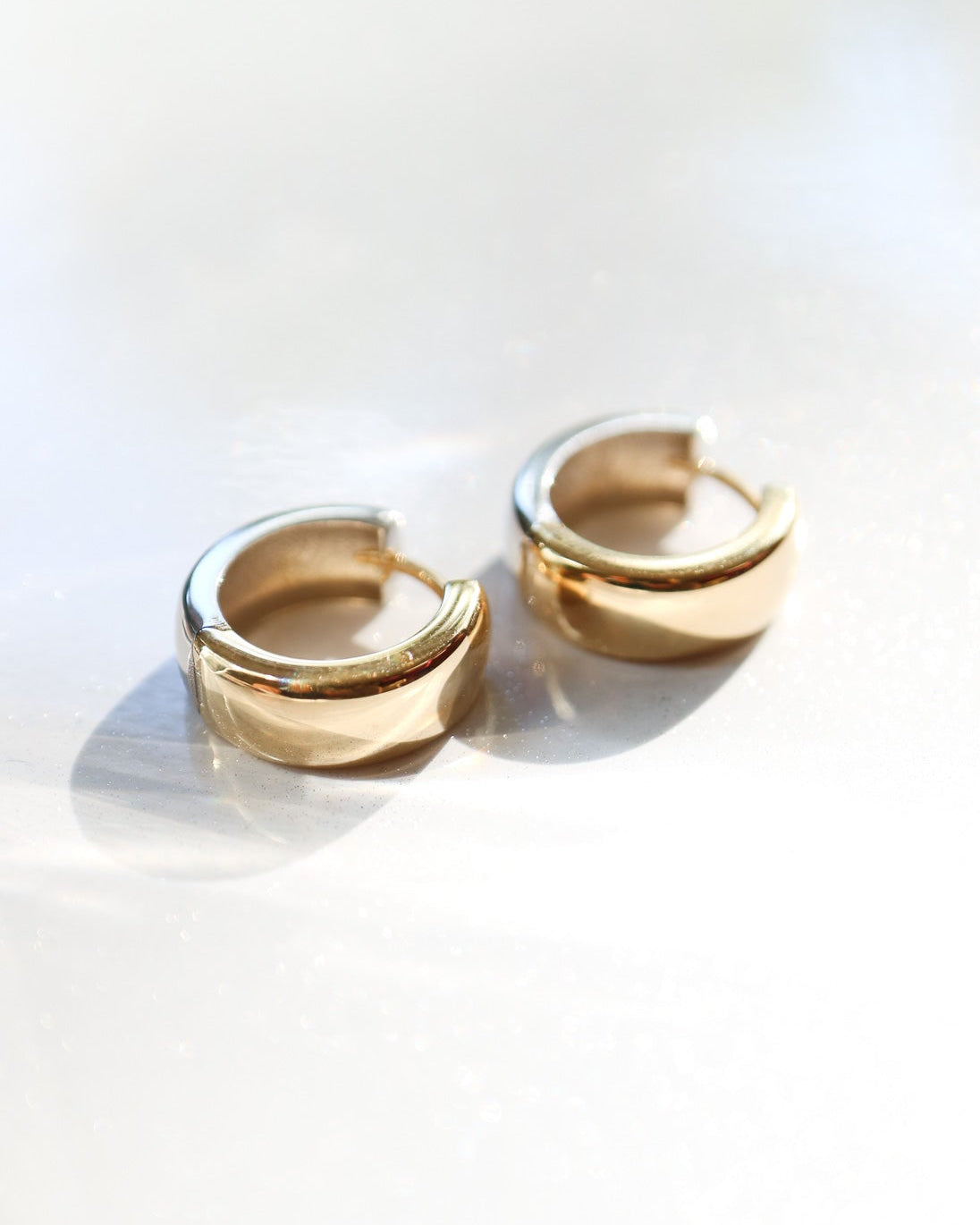 9kt solid gold Two Tone Hoops featuring a contemporary rounded design with contrasting polished gold and silver tones, photographed on a white background with soft sunlight and shadows.