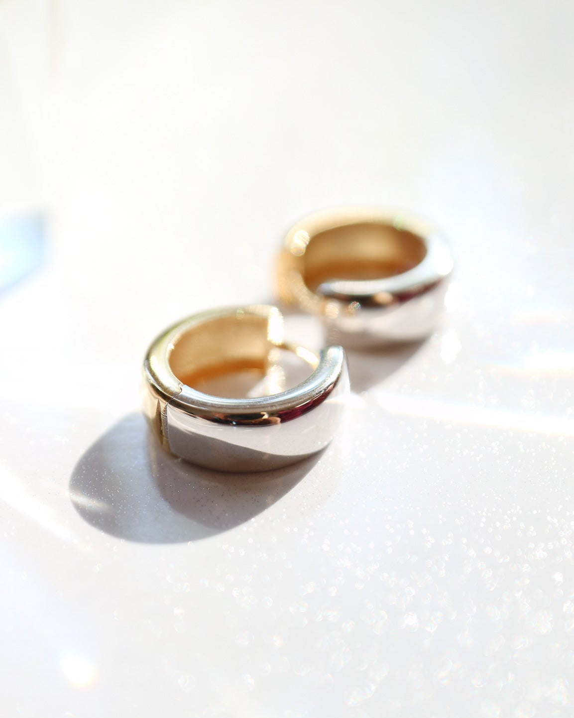 9kt solid gold Two Tone Hoops featuring a contemporary rounded design with contrasting polished gold and silver tones, photographed on a white background with soft sunlight and shadows.