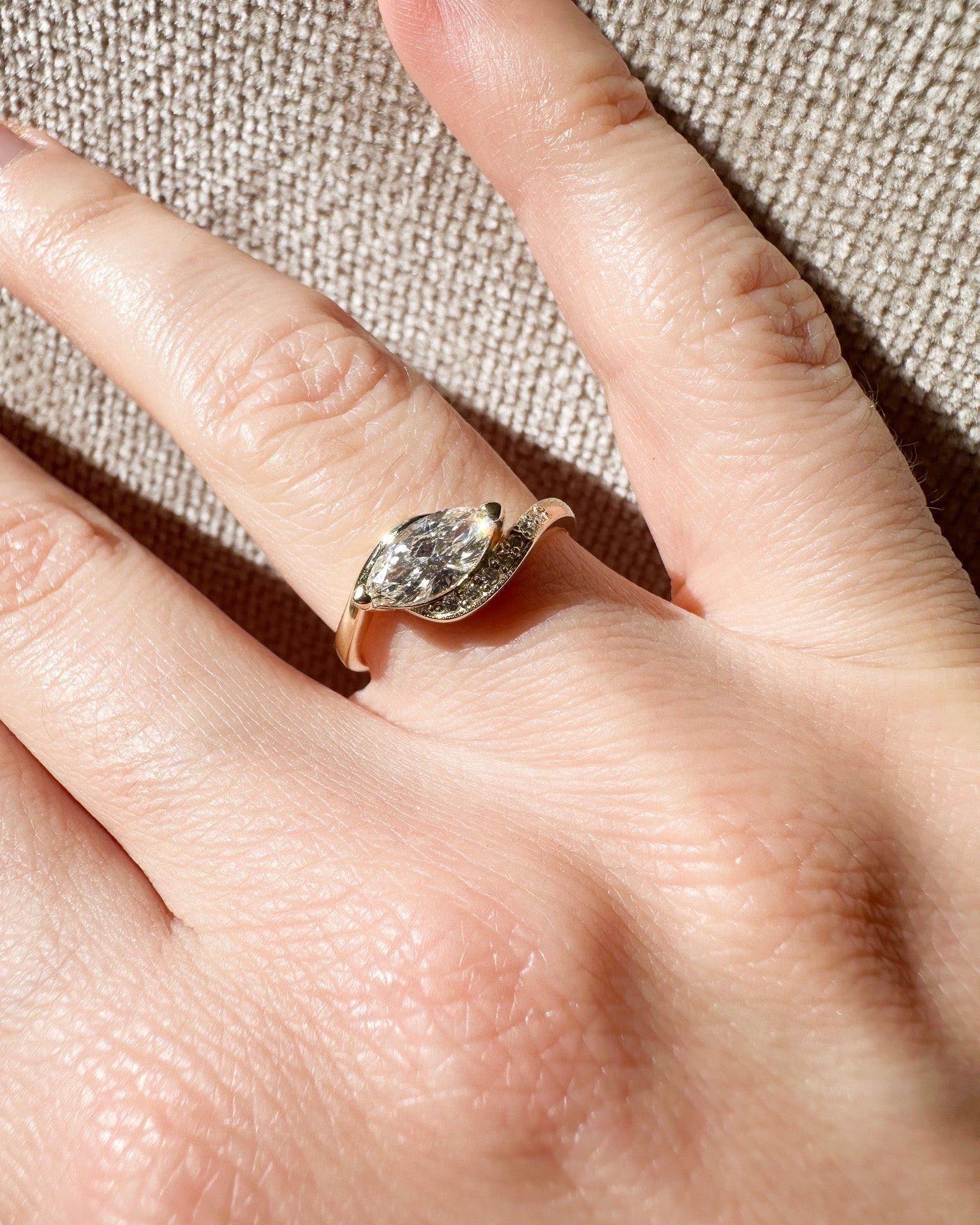 Gold ring with a marquise-shaped diamond on a hand against a textured beige background