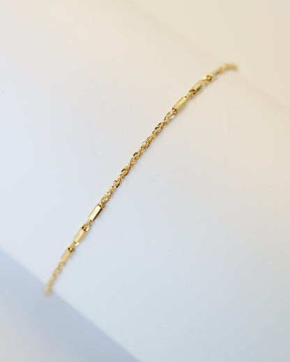 9kt solid gold Morse Code Chain bracelet featuring a delicate gold chain with polished rectangular bar accents, photographed on an off-white background.