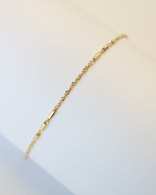 9kt solid gold Morse Code Chain bracelet featuring a delicate gold chain with polished rectangular bar accents, photographed on an off-white background.