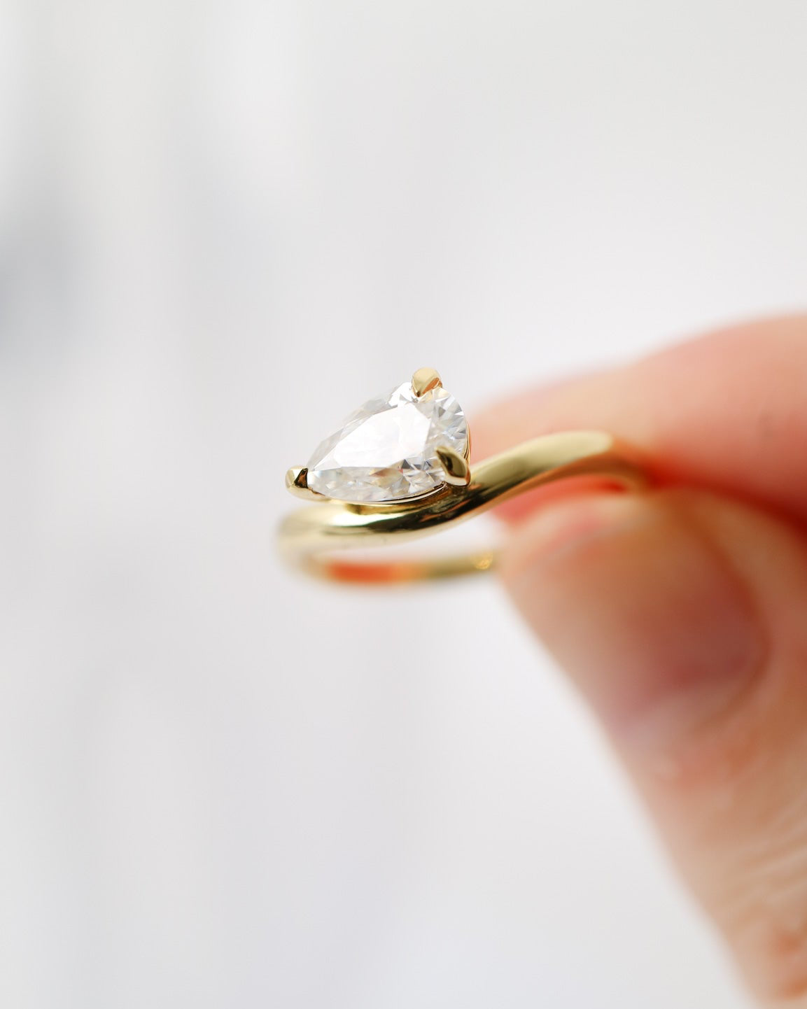 Gold ring with a clear gemstone held by a hand on a light gray background