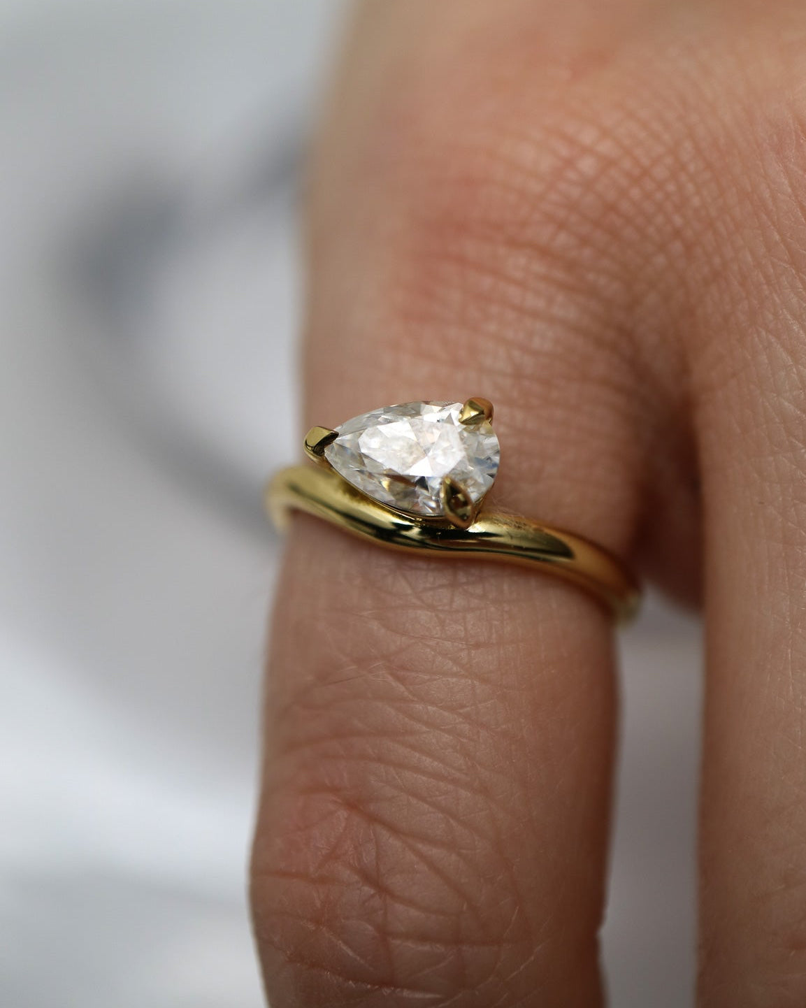 Gold ring with a pear-shaped diamond on a finger against a neutral background