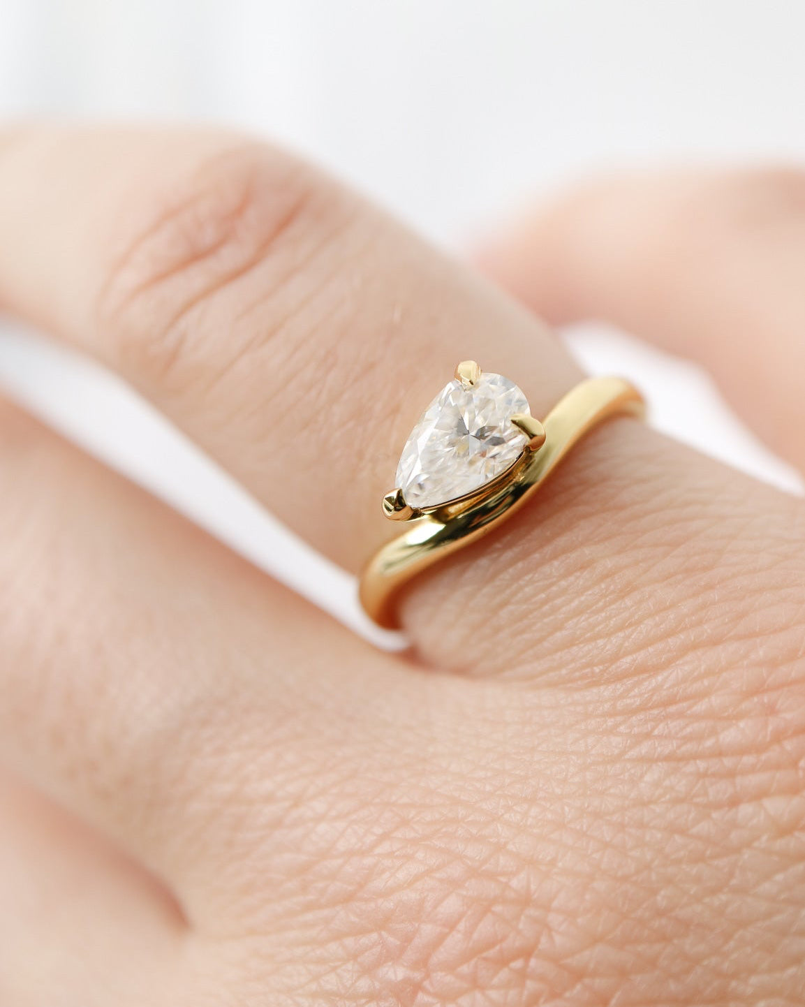 Gold ring with a pear-shaped diamond on a finger against a white background