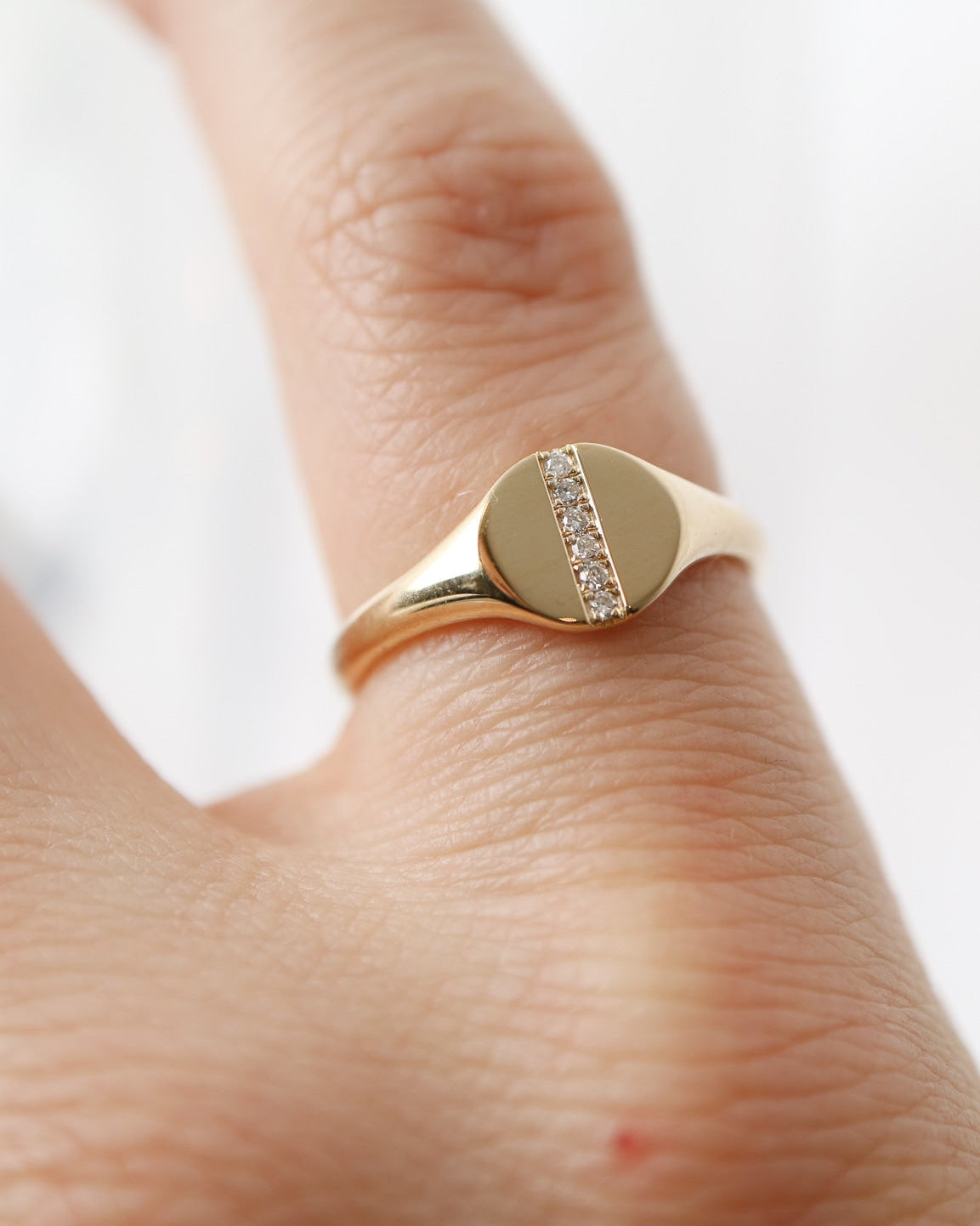 Gold ring with a circular design on a person's finger against a white background