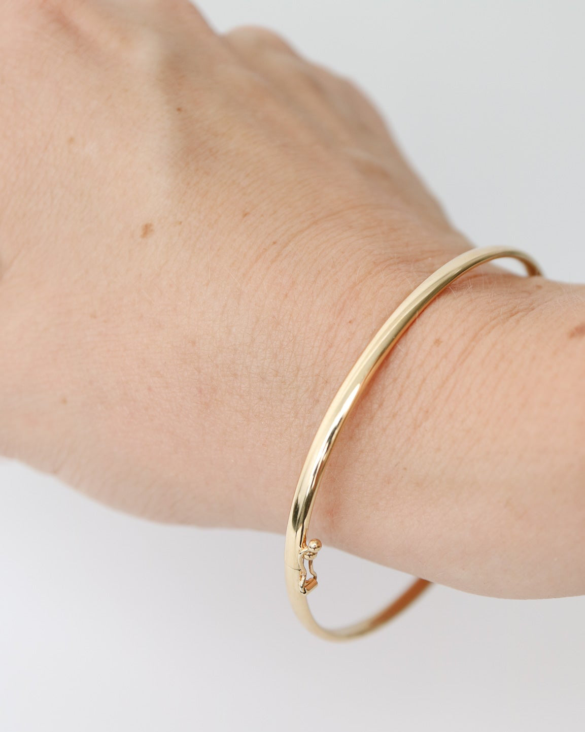 9kt solid gold Classic Oval Bangle with a polished finish, lightweight hollow construction and flexible design, photographed on a female wrist.
