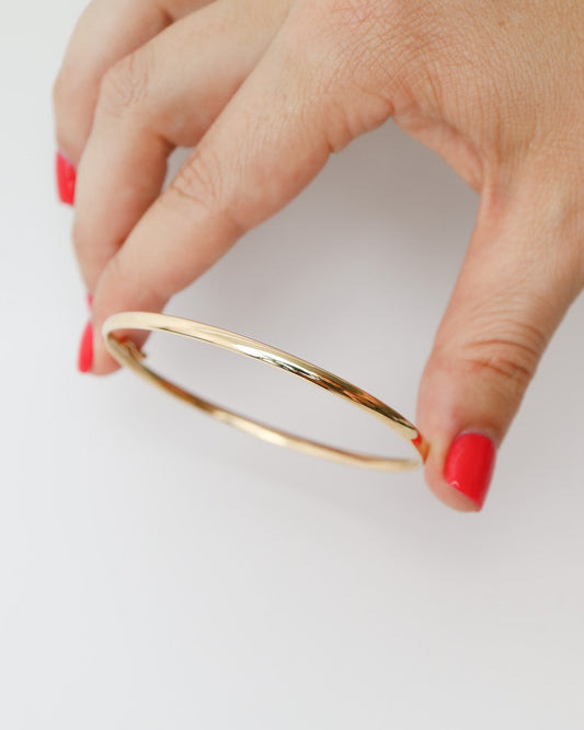 9kt solid gold Classic Oval Bangle with a polished finish, lightweight hollow construction and flexible design, photographed on a white background and held in female fingers