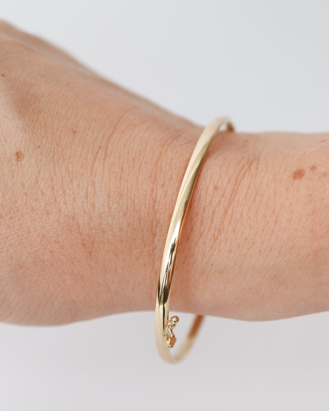 9kt solid gold Classic Oval Bangle with a polished finish, lightweight hollow construction and flexible design, photographed on a white background on a female wrist