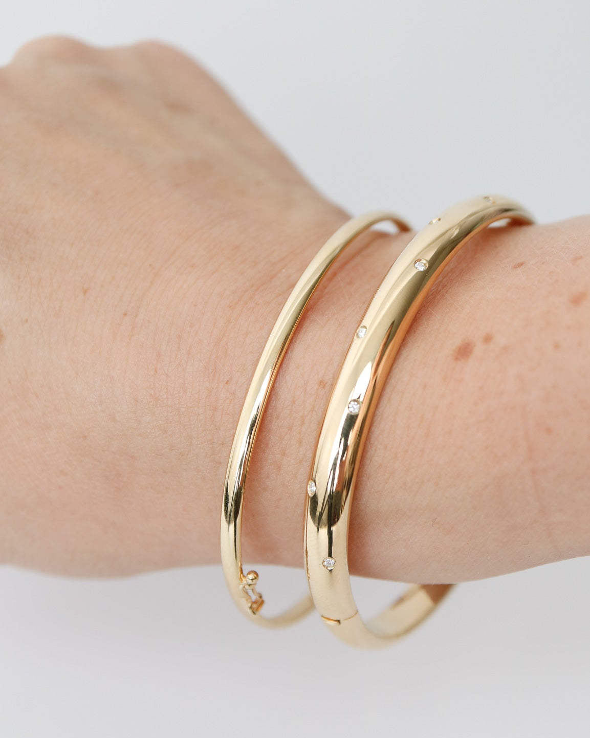9kt solid gold Classic Oval Bangle with a polished finish, lightweight hollow construction and flexible design, photographed stacked with a wider 9kt gold and diamond bangle