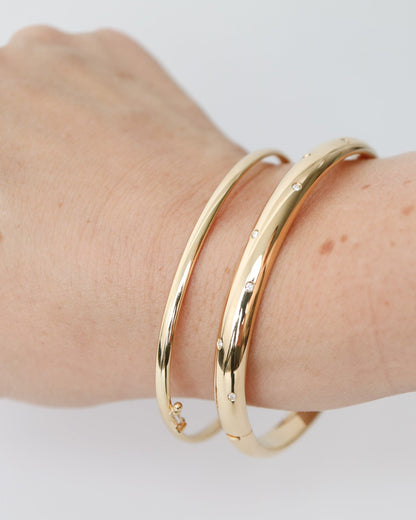 9kt solid gold Classic Oval Bangle with a polished finish, lightweight hollow construction and flexible design, photographed stacked with a wider 9kt gold and diamond bangle
