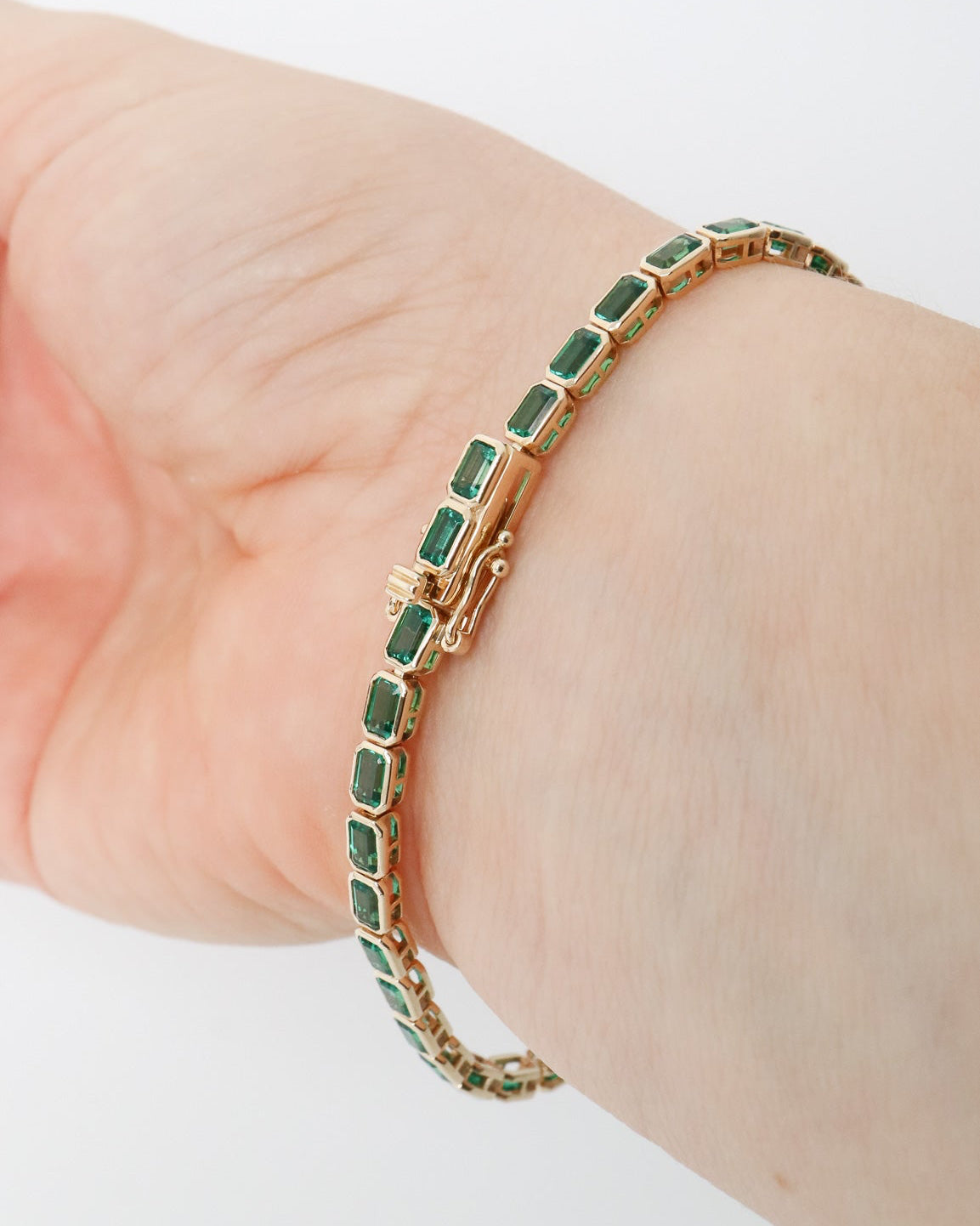 Gold bracelet with green stones on a wrist against a white background
