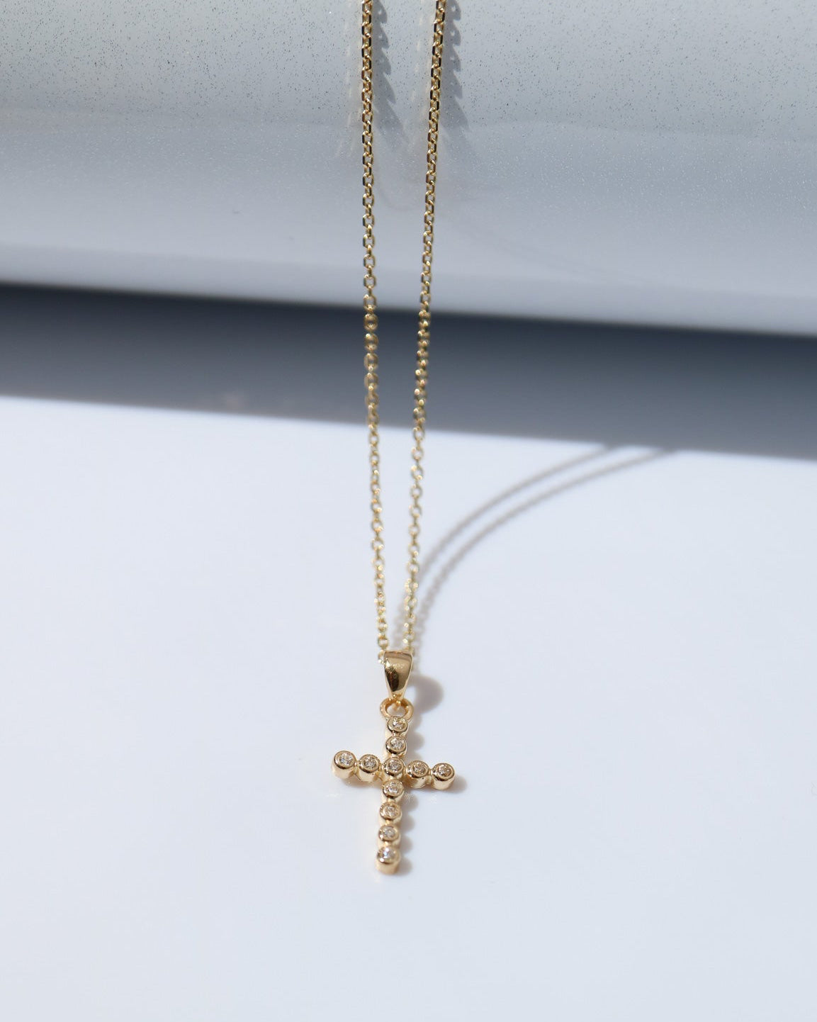 Gold cross necklace on a light gray background