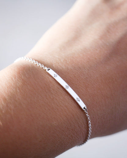 Silver bracelet with engraved stars on a wrist against a neutral background