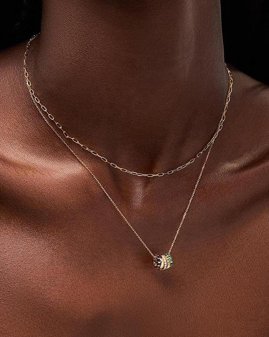 Gold necklace with a green pendant on a model against a neutral background