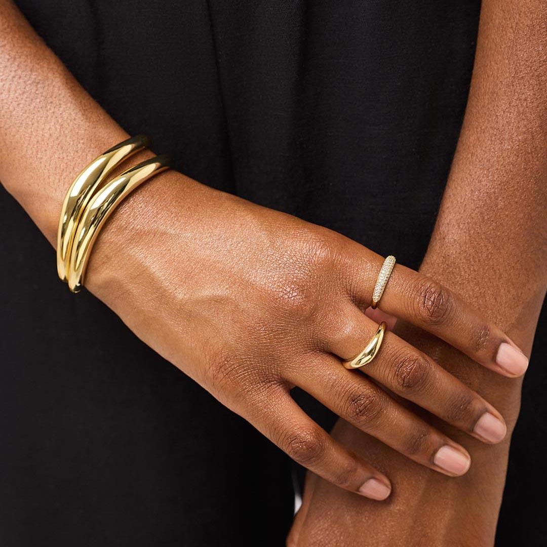 Hand wearing a gold bracelet and ring on a black background