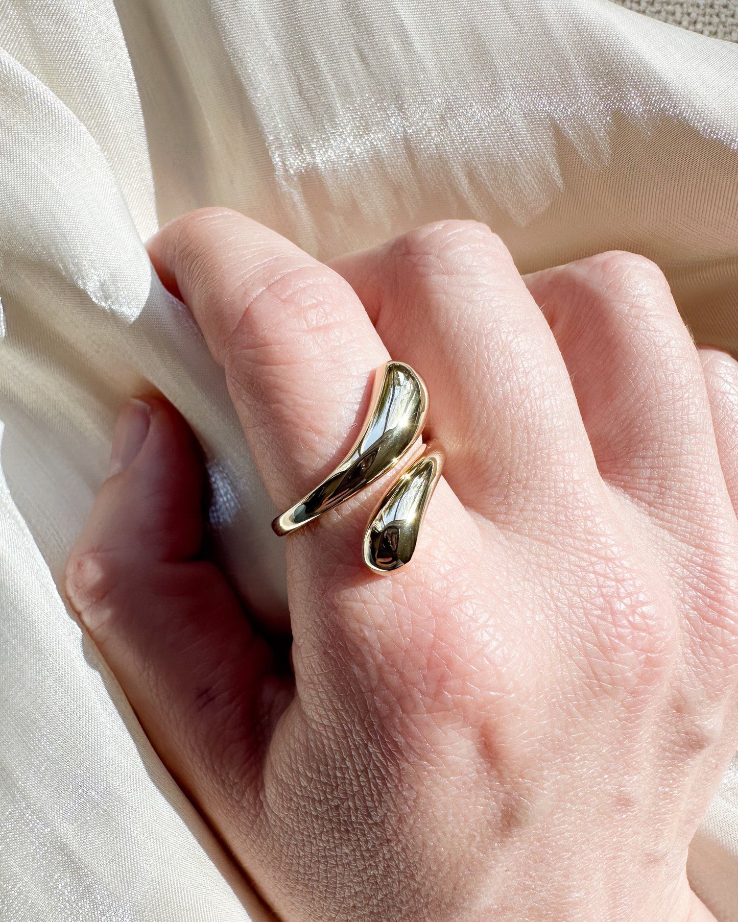 Gold ring on a person's finger with a soft white fabric background