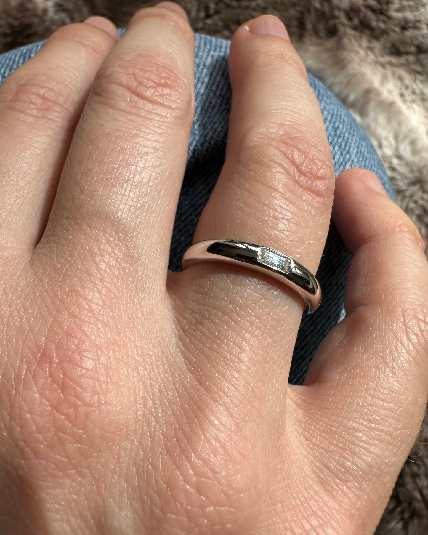 Hand wearing a silver ring on a textured fabric background