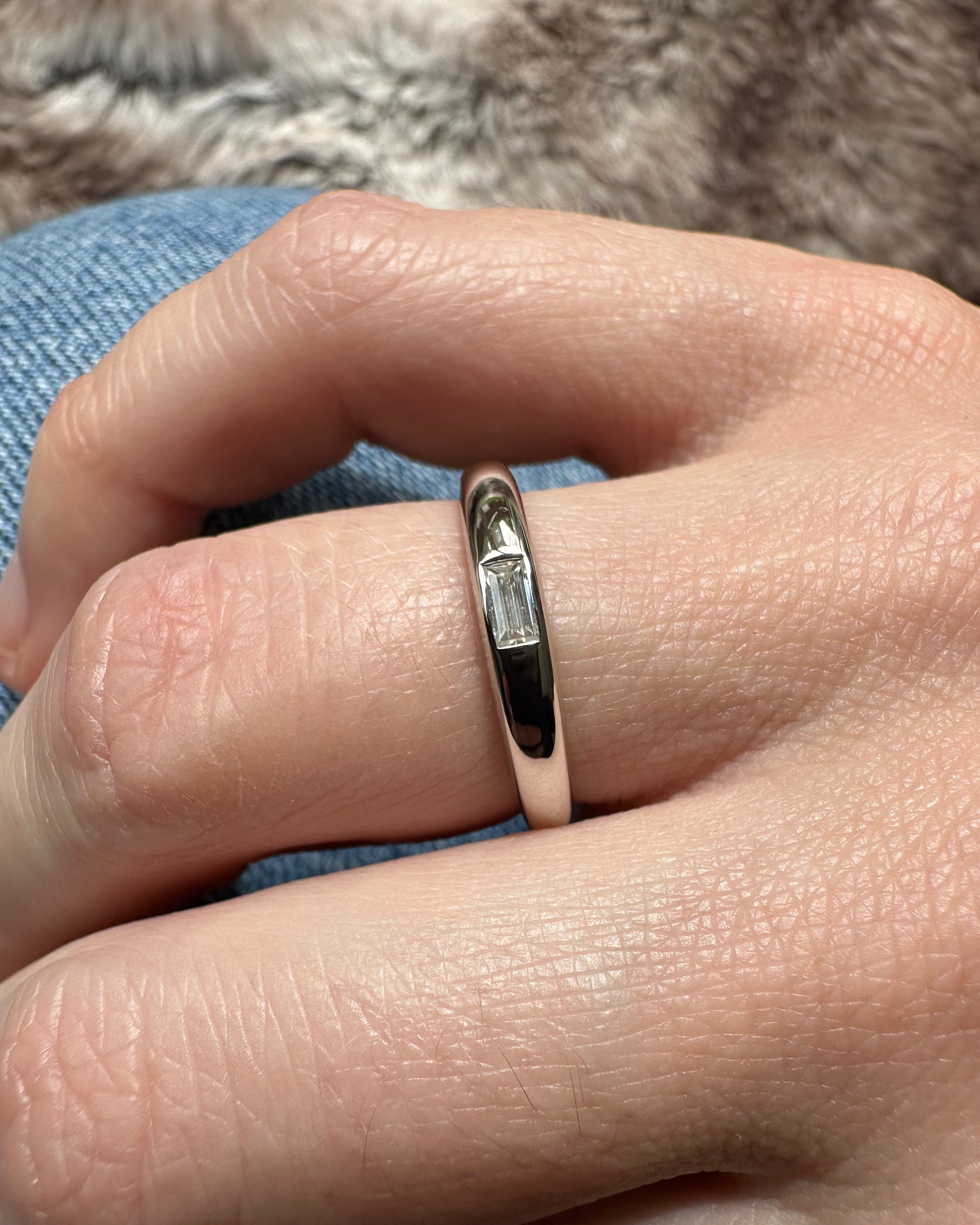 Hand wearing a ring with a diamond on a textured fabric background