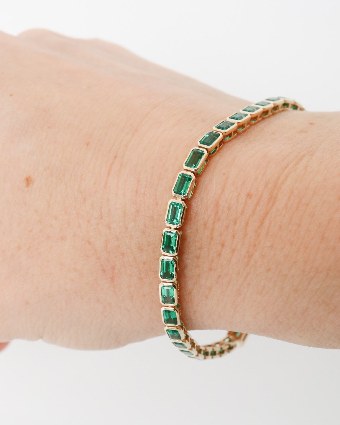 Gold bracelet with green gemstones on a wrist against a white background