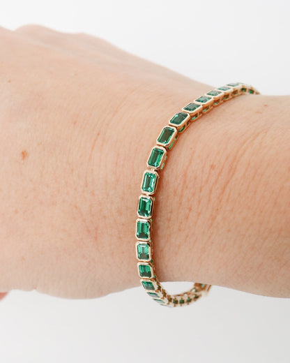 Gold bracelet with green gemstones on a wrist against a white background