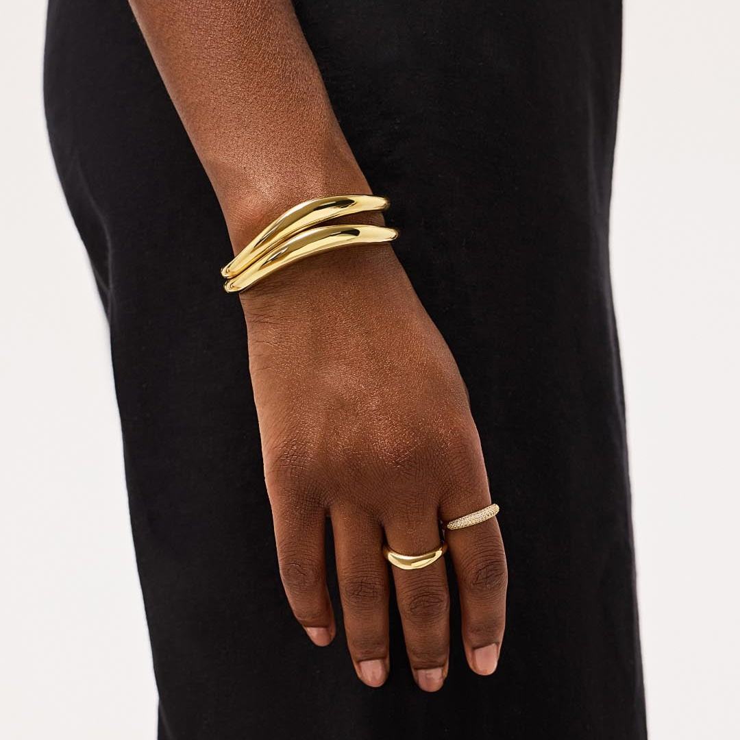 Gold bracelet and ring on a person's wrist against a black background