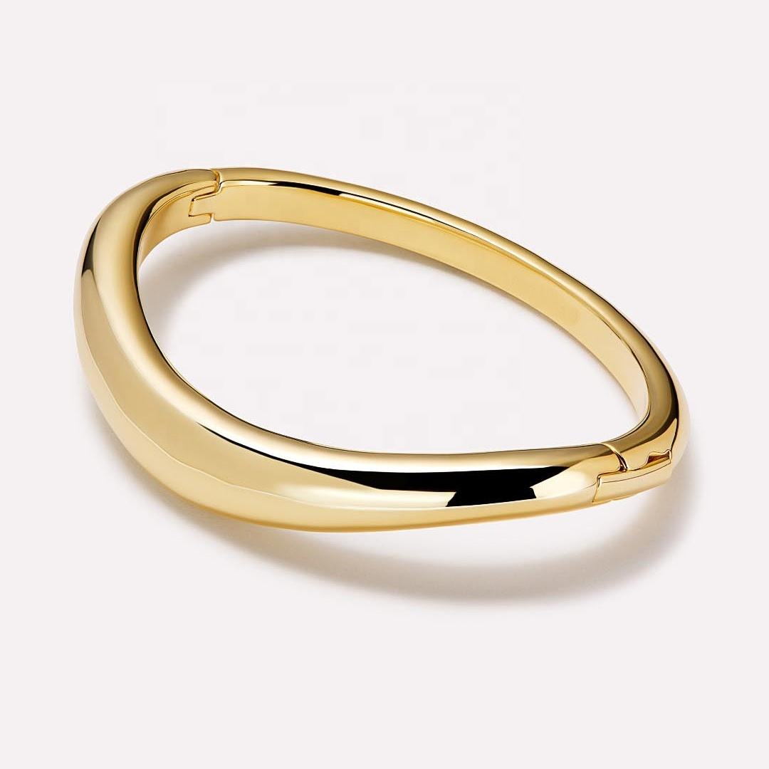 Polished sculptural gold bangle with an organic curved silhouette and hinged closure on a soft neutral background.
