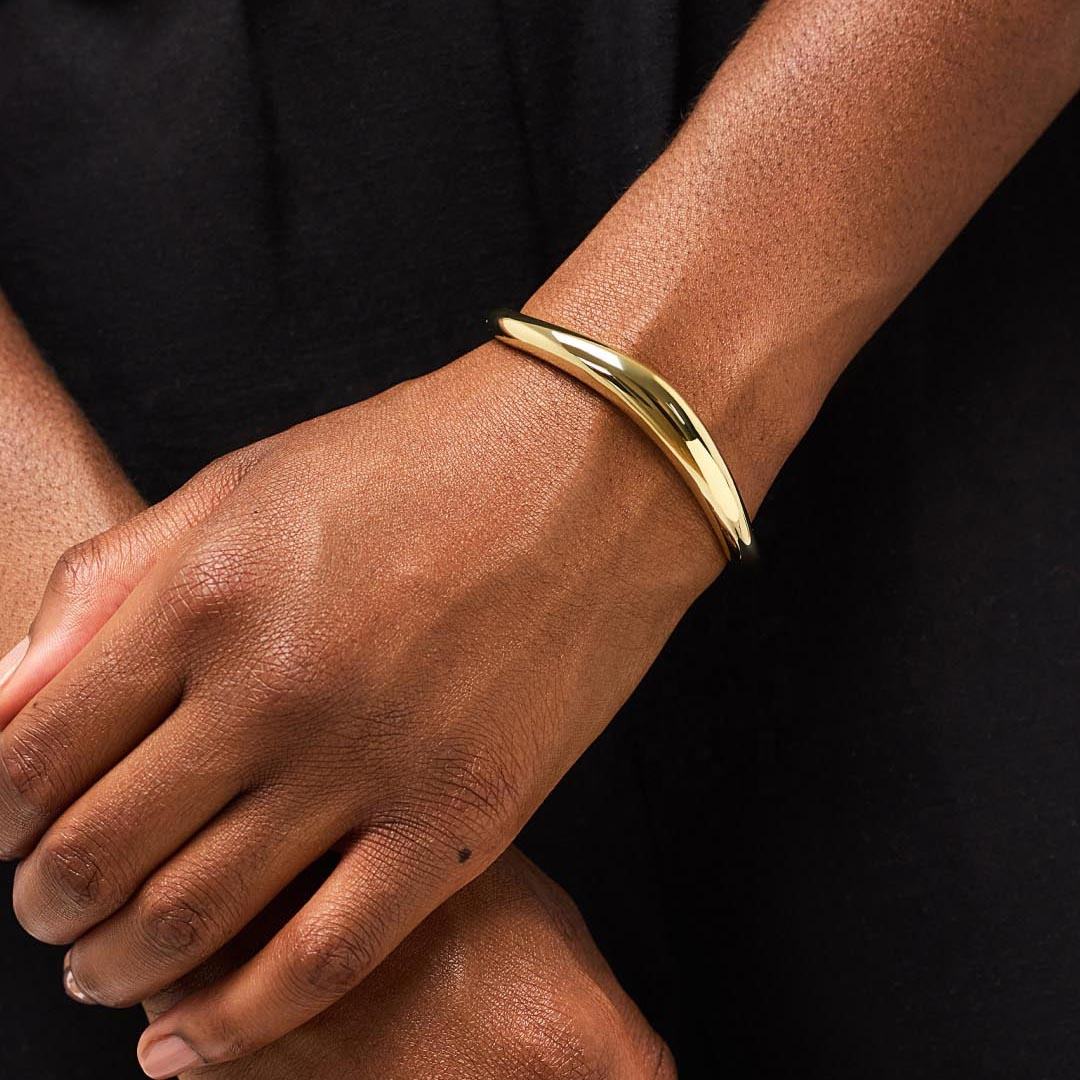 Gold bracelet on a person's wrist with a black background