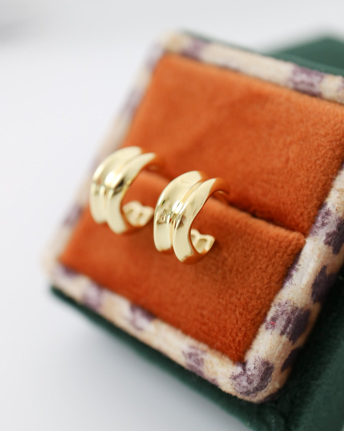 Gold crescent moon earrings on an orange fabric surface with a green box background