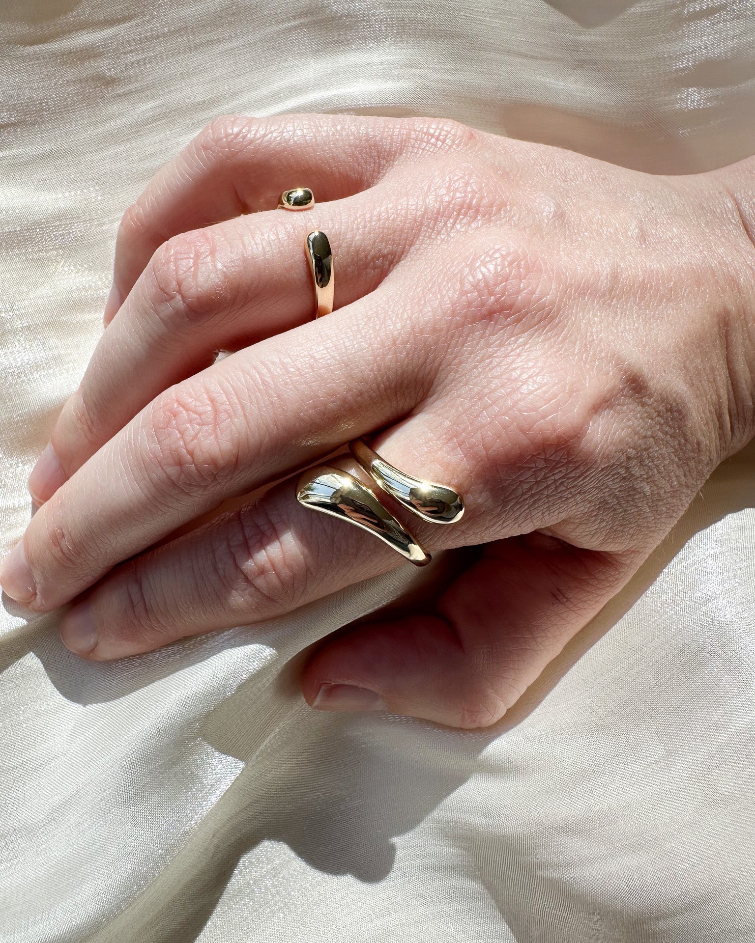 Close-up of a hand wearing two gold rings on a light background